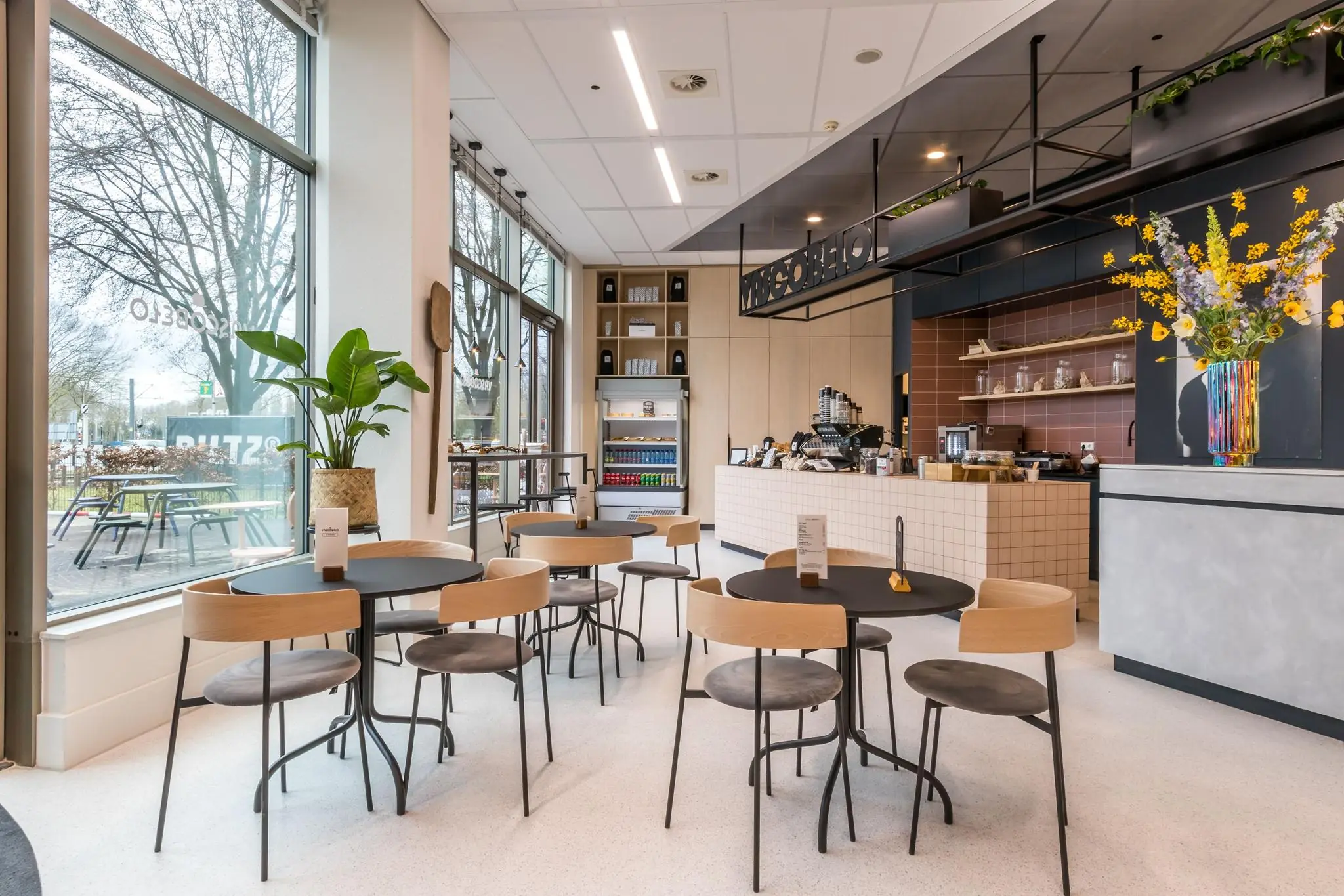 Modern ingericht café aan de Vliegend Hertlaan met grote ramen, minimalistische meubels en een gezellige koffiebalie.